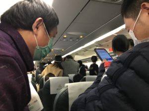 Chinese air passengers in masks take video of something going on in the back of the plane.