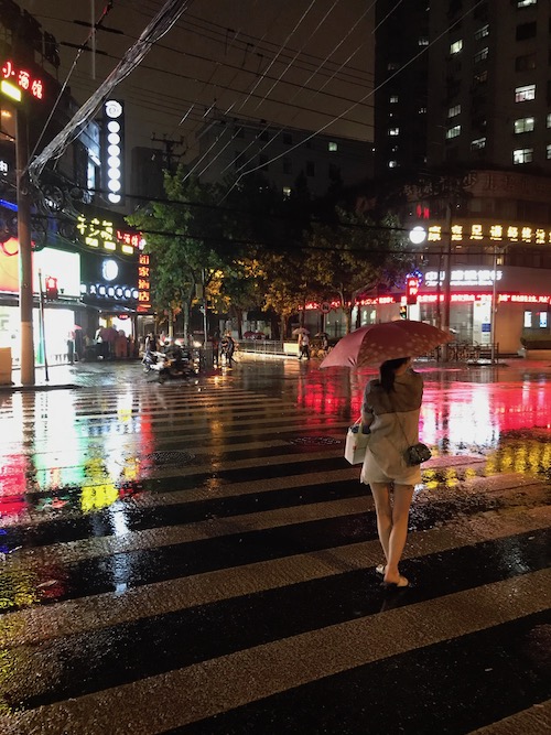 A woman walks in the rain in Shanghai - Is the water in China safe? onaroadtonowhere.com