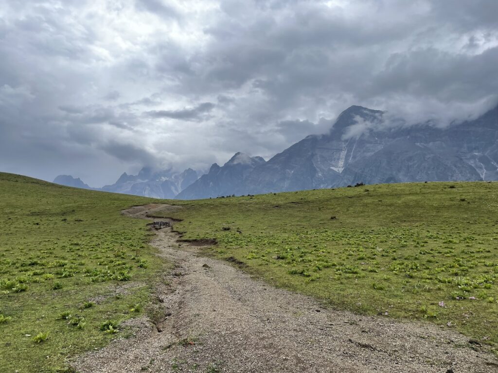 Path through a meadow leading to cloudy mountain peaks at Jade Dragon Snow Mountain