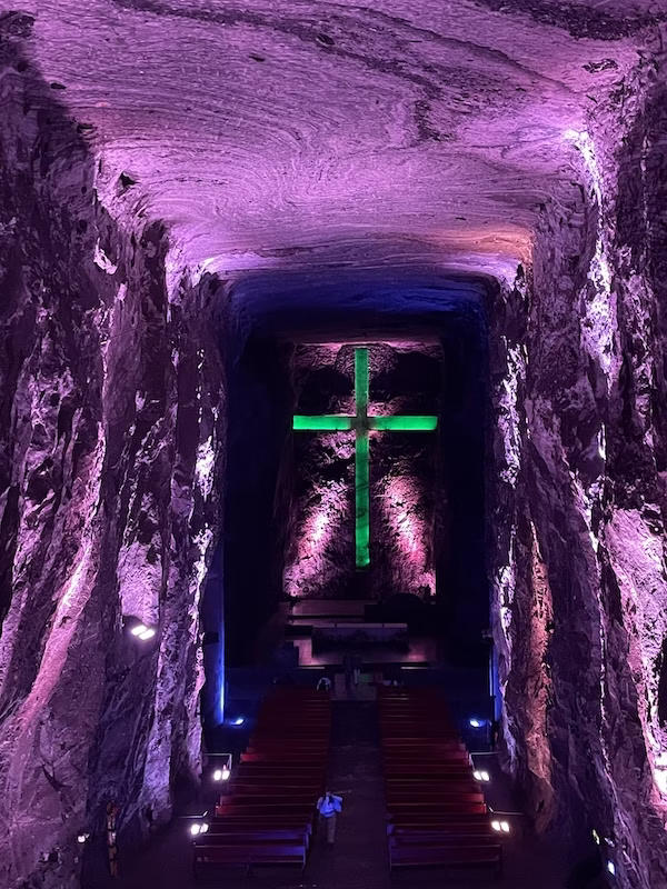A green lit cross in a purple lighted cavernous space in the Salt Cathedral of Zipiquirá, Colombia
