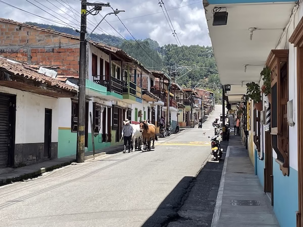 A man walks two horses down a city street in Jardín, Colombia