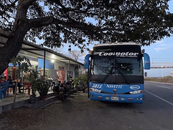 A blue bus broken down on the side of the road.