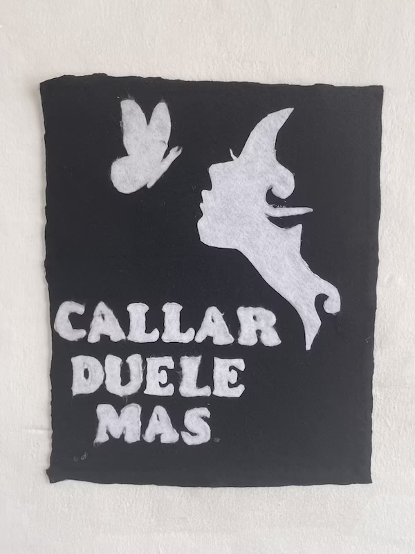 A fabric art work that says "callar duele mas" or "being quiet hurts more"