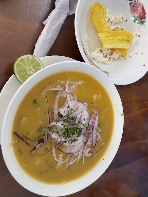 A bowl of encebollado accompanied by popcorn and a fried plantain.