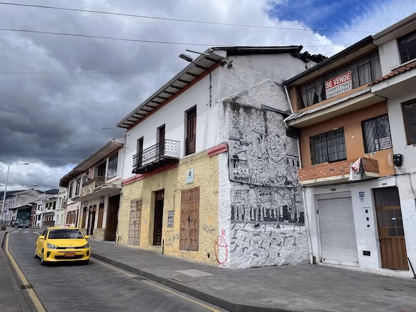 A yellow taxi drives down the street in Cuenca, Ecuador in front of Spanish Colonial buildings