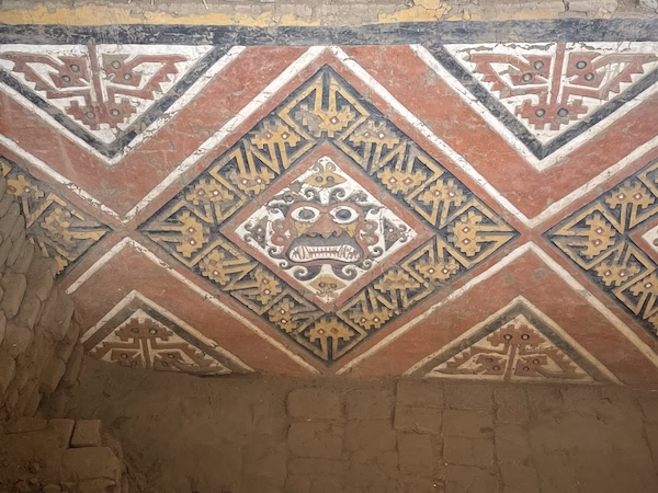 Painting in red, yellow and white of an angry face found inside the Temple of the Moon, a temple built by the Moche culture in Peru