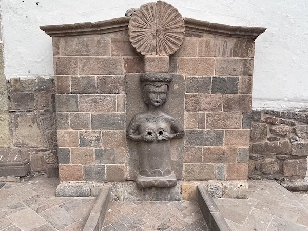 An ancient fountain sculpture depicting a topless woman holding her breasts