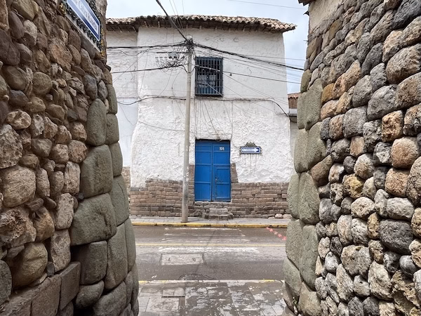A  white Spanish colonial building with a blue door in between two Inca stone walls