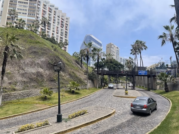 Cars drive on a road below the green cliffs and highrises in Lima