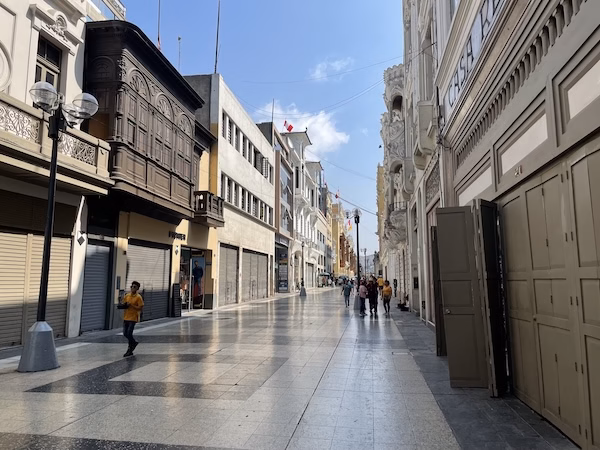 Peruvians walk down a pedestrian only street between colonial buildings in Lima