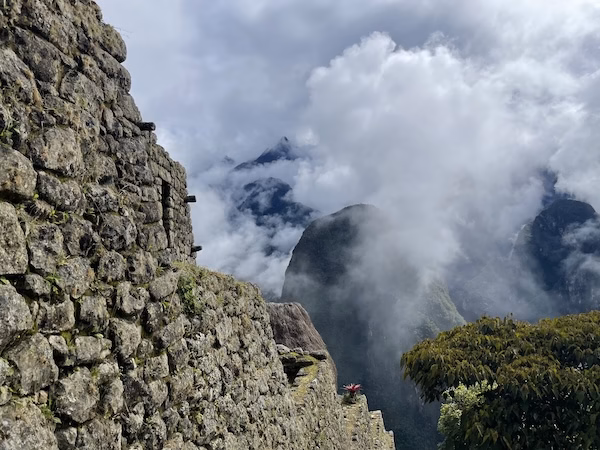 A wall overlooking a cliff and surrounding clouds at Machu Picchu
