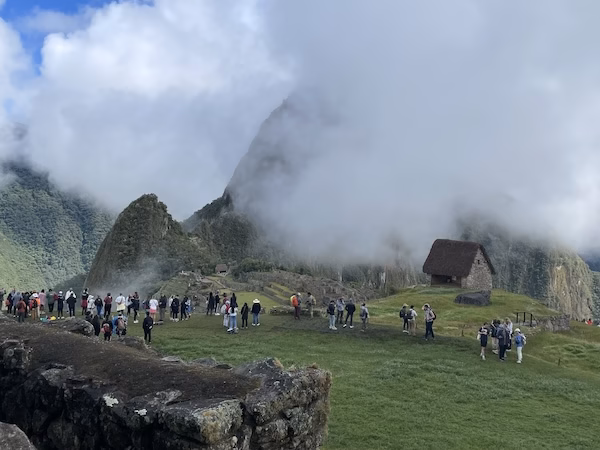 A crowd of tourists stands in front of a misty mountain at Machu Picchu