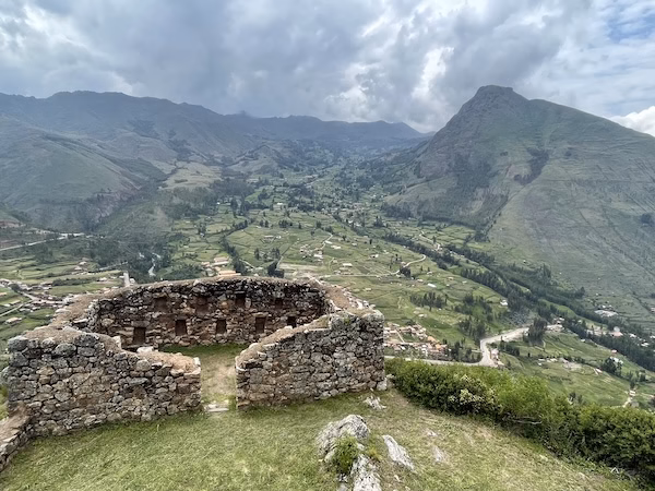 Inca stone walls overlook a green, mountainous valley in Pisac