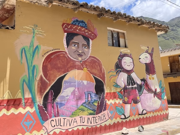 A mural featuring an Inca woman, a child and a llama that says "cultivate your interior" on a wall in the Sacred Valley of Peru