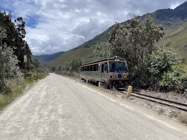 A train car drives next to a roadway near Ollantaytambo in the Sacred Valley of Peru